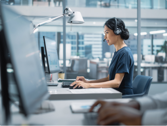 Image of a lady working on a desktop computer with a headset on 