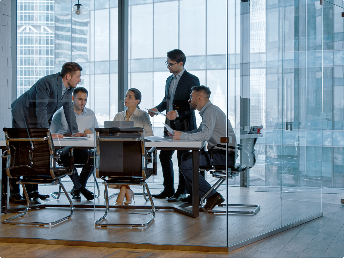 Image of people surrounding a table in a glass walled meeting room having a discussion