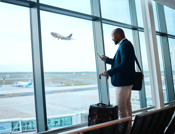 Man on his phone at the airport at the window and a plan taking off