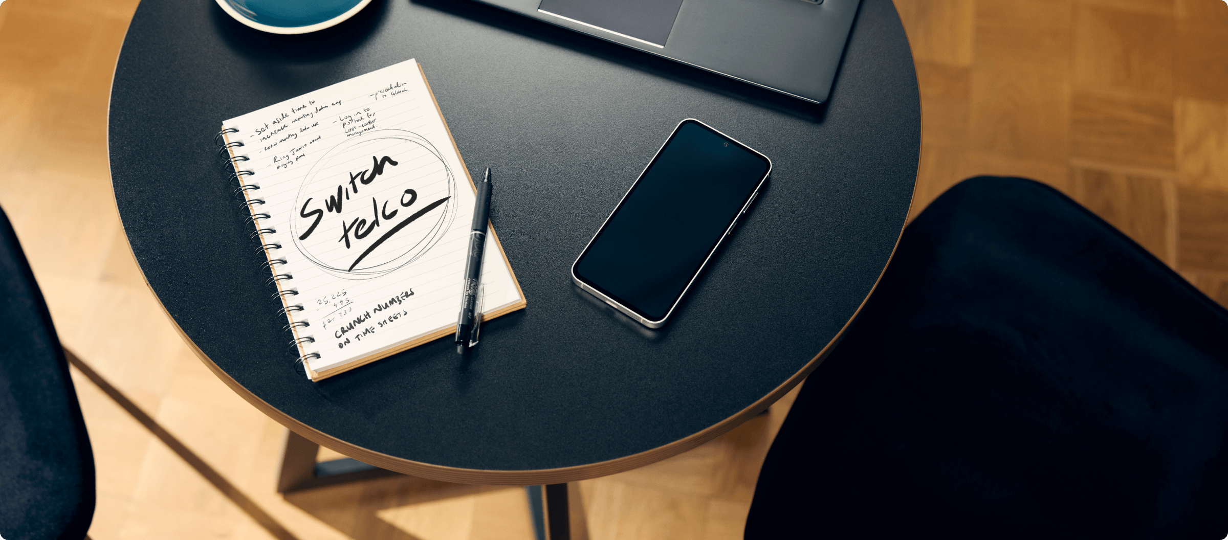 Image of a table with a mobile phone and a notebook with "Switch Telco" written inside