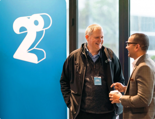 Image of two men talking in front of the 2degrees logo banner