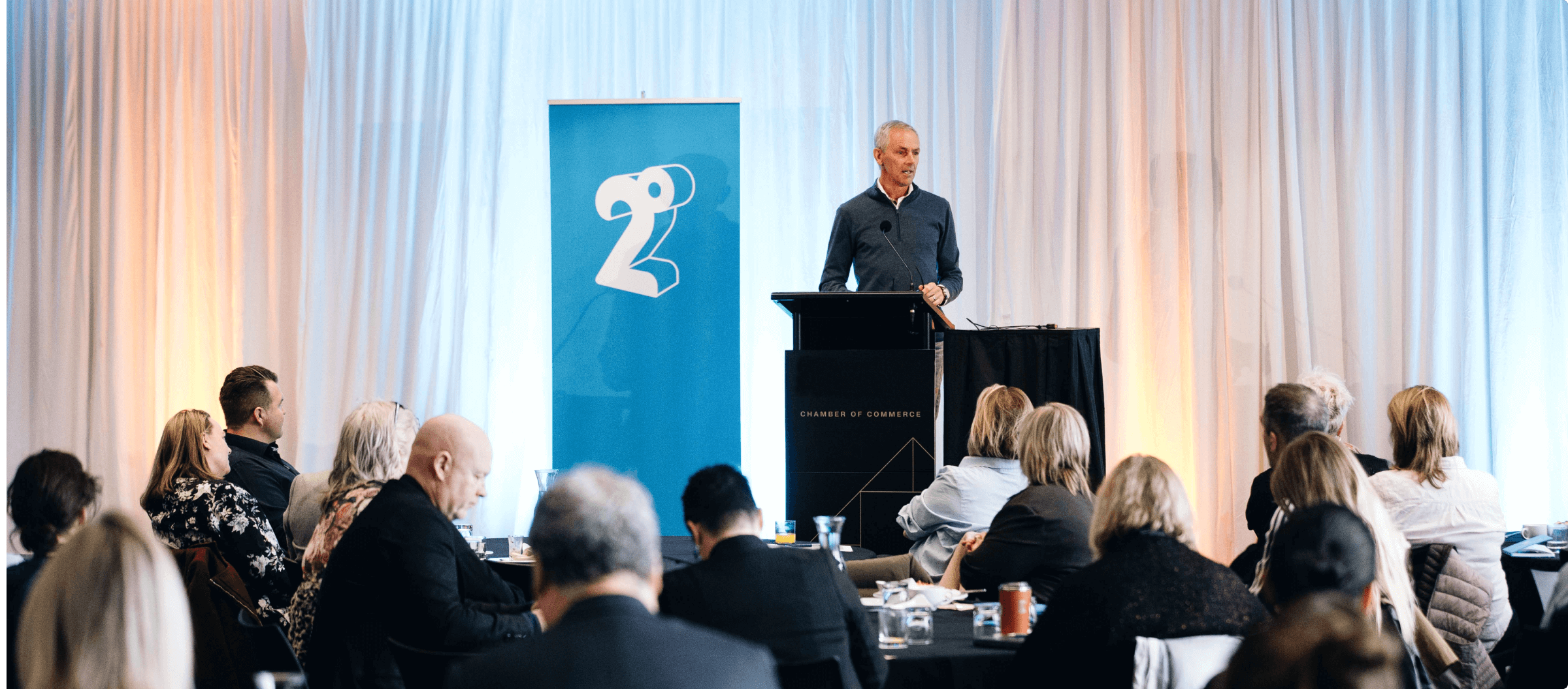 Photo of man standing at lectern at a conference with 2degrees and Chamber of Commerce branding