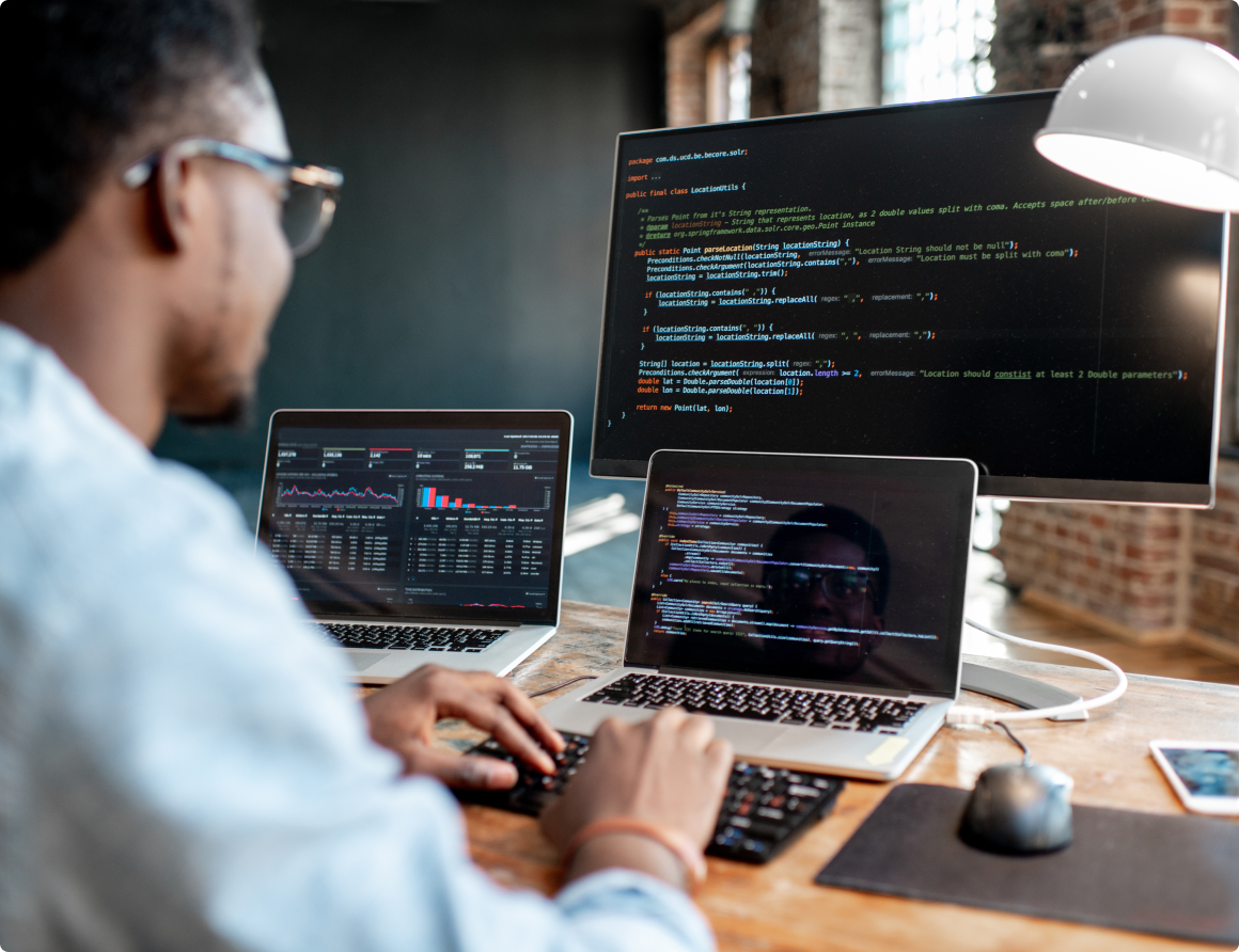 male programmer writing program code sitting at the workplace with three monitors in the office