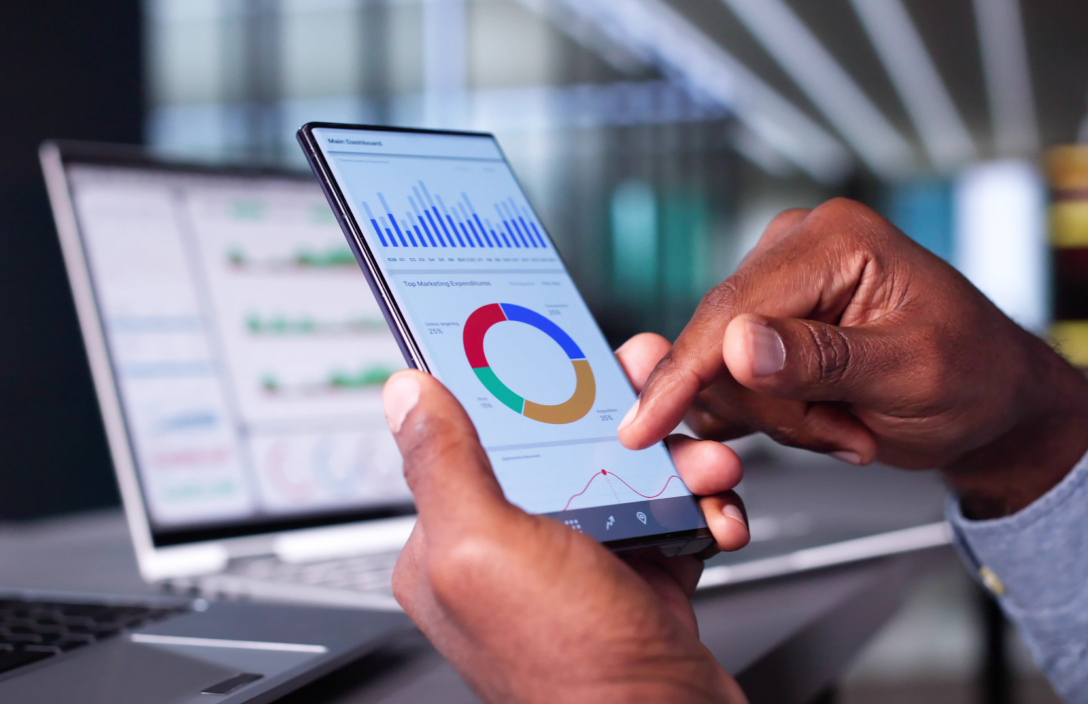 Man holding a mobile phone showing a analytics dashboards and graphs on a mobile phone