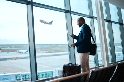 Man on his phone at the airport at the window and a plan taking off