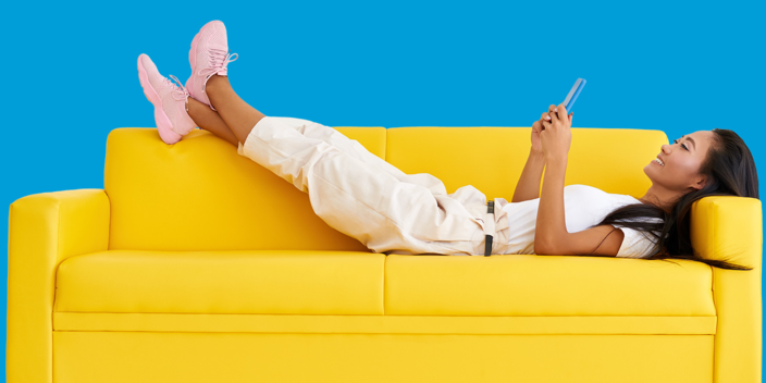 Woman lying on a yellow couch with her feet up playing on her mobile phone